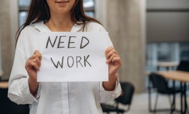 Manzarayı kapat. Görevdeki genç kadın, üzerinde çalışma gereksinimi yazılı pankart taşıyor..