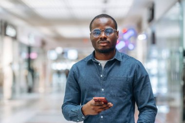 Ön manzara, elinde akıllı telefonla. Siyah adam süpermarketin holünde..