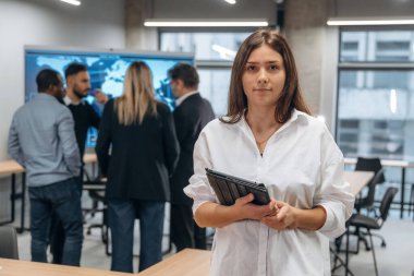 Bir kadının elinde not defteri. Bir grup ofis çalışanı içeride birlikte..