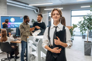 Kadın meslektaşlarının önünde duruyor. Ofiste 3D yazıcının yanında insanlar var..