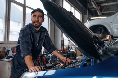 Şapkadayım, meşgulüm. Araba tamirhanesinde çalışan bir tamirci..