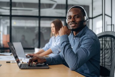 Kulaklıkla ve dizüstü bilgisayarlarla. Çağrı merkezinde insanlar çalışıyor..