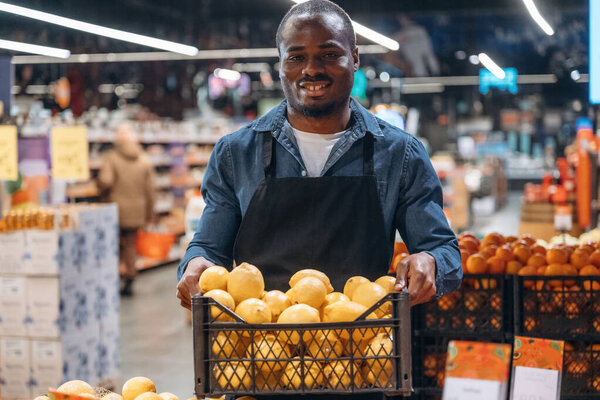 Fresh fruits. Grocery store worker in apron is near products.