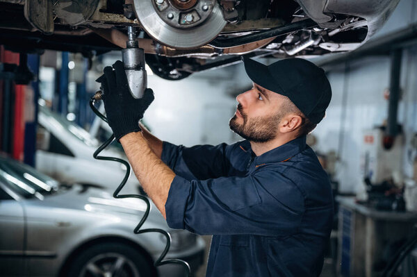 Automobile is up, hanging. Mechanic working in a car service station.