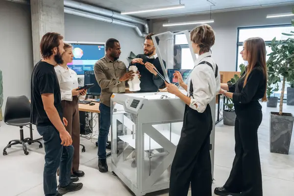 Toplanıyor, basılı ürünlere bakıyor. Ofiste 3D yazıcının yanında insanlar var..