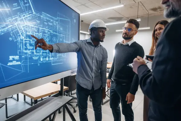 İnşaat planı ekranda. Bir grup ofis çalışanı içeride birlikte..