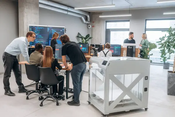 Duvarında kod olan büyük ekran. Ofiste 3D yazıcının yanında insanlar var..