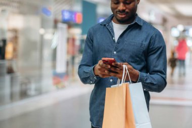 Kırmızı akıllı telefon ve el çantaları. Siyah adam süpermarketin holünde..