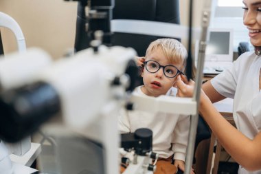 Yeni gözlüklerle. Küçük çocuk göz doktorunun dolabını kontrol ediyor..