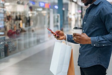 Akıllı telefondan interneti kaydırmak. Süpermarketteki alışveriş çantalı adamın yakın görüntüsü..