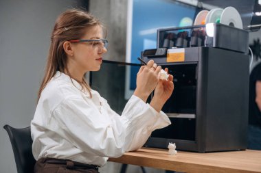 Bilgisayarla, oturarak. Kadının elinde 3D yazılı oyuncak kaplumbağa var..