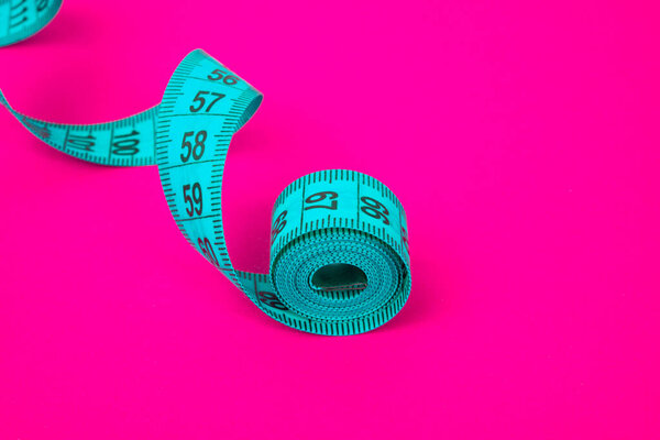 Blue tape measure on pink paper background diet concept