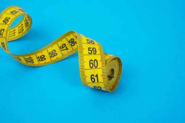 Yellow tape measure on blue paper background diet concept