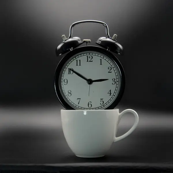 A cup and retro alrm clock on black background. Spending time drinking hot drinks.