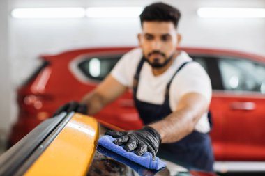 Sakallı, araba yıkayan, koruyucu eldiven takan, lüks, sarı pencereleri ön cam kullanarak temizleyen bir adama odaklan. Araba temizleme veya araç konsepti.