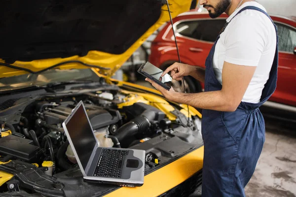 タブレットコンピュータを使用して整備士の作物ビュー 自動車エンジンのチェックを記録することは 車のワークショップでの彼の仕事中に詳細情報を収集します エンジン修理中の保守サービス — ストック写真