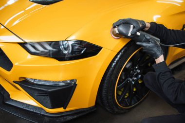 Auto detailing service, polishing of the car. Close up view of hands of man worker, polishing hood and body of modern yellow luxury car with orbital polisher and wax. clipart