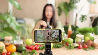 Güzel Asyalı genç kadın blogcu akıllı telefondan sağlıklı salatanın organik taze sebzeler ve meyvelerle nasıl pişirileceği ve çevrimiçi yemek pişirme konsepti hakkında video dersi alıyor..