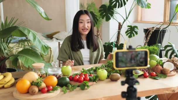 年轻的亚洲女性博客作者或内容创建者准备平滑和记录视频的电话 迷人的女性一边在时尚厨房用手机记录博客 一边展示如何烹调健康食品 — 图库视频影像