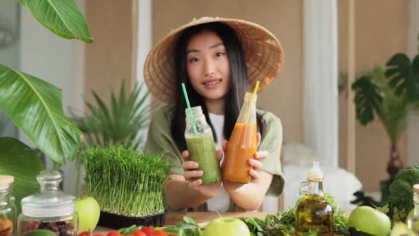 熱帯エキゾチックなキッチンで朝食のための健康的な新鮮なスムージーを準備魅力的な若いアジアのビーガン女性 2本のボトルを手に持つ魅力的な女性 緑の健康食品のコンセプト — ストック動画