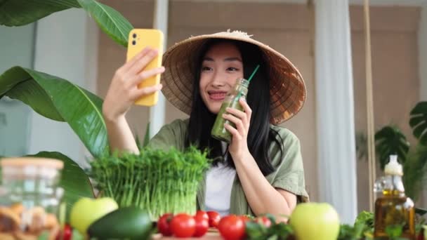 伝統的な円錐形の帽子の楽しいアジアの女性は 健康的なディナーを楽しんだり ビデオ通話をしたり 熱帯リゾートのエキゾチックな光スタジオで自撮りをしたりします 減量のための食品や栄養 — ストック動画
