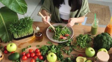 Kadınların eli kapalı taze sağlıklı vegan salatasını taze organik sebzelerle karıştırıyor. Tropik egzotik mutfakta ahşap kaşık kullanıyor. Stüdyo evde yeni bir tarif deniyor..