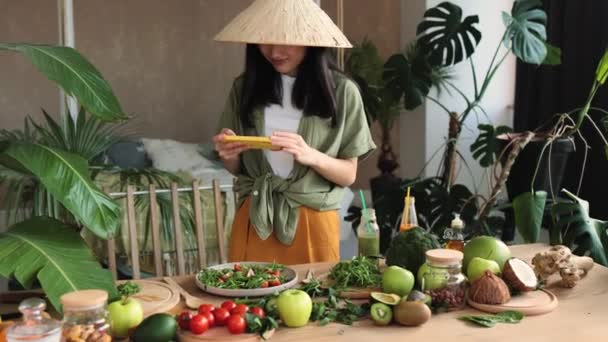 아시아인 블로거 스마트폰으로 미디어에 사진을 올리고 부엌에 전통적 이국적 집에서 — 비디오