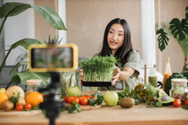 レシピについてのスマートフォンでビデオレッスンを記録する美しい若いアジアの女性ブロガーマイクログリーンもやしや有機新鮮な野菜や果物から健康的なサラダを調理する方法 — ストック写真