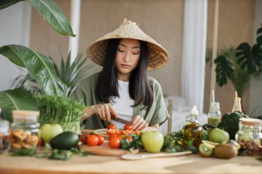 Genç Asyalı kadın blogcu ya da domates doğrayan içerikli yaratıcı vegan salatası hazırlıyor ve telefonda video kaydediyor. Akıllı telefonla blog kaydederken sağlıklı yemek pişiren çekici bir kadın.