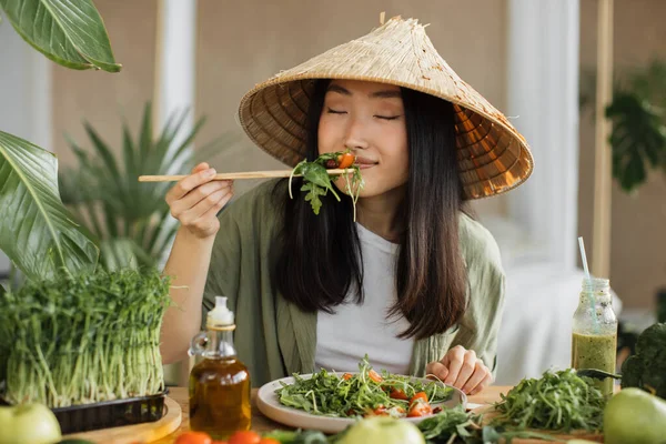 伝統的な円錐形の帽子の陽気でかわいい幸せな若いアジアの女性は 熱帯エキゾチックなリゾートのテーブルの上に座って健康的なサラダを食べています 緑の健康的なビーガンフードコンセプト — ストック写真
