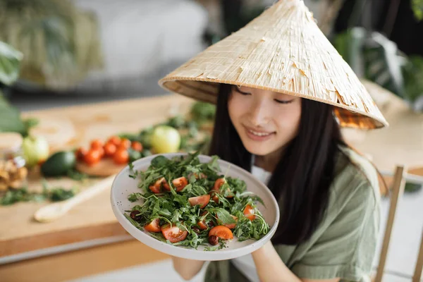トロピカルリゾートのエキゾチックな光スタジオで健康的なディナーを楽しむ有機野菜から健康的なサラダを保持している伝統的な円錐形の帽子の楽しいアジアの女性 減量のための食品や栄養 — ストック写真