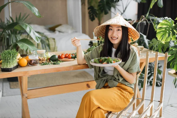 有機野菜とテーブルの近くに座っている間にベジタリアンサラダを保持している若いアジアの女性の肖像画 健康的な食事を楽しみます 光エキゾチックなキッチンスタジオのインテリアで屋内 減量の概念 — ストック写真