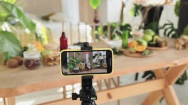 Blogcu ya da içerik yaratıcısı evde doğal kozmetik ürünleri hazırlıyor ve telefonda video kaydediyor. Kivi, portakal, naneli hindistan cevizi derisi ve kaplıca. Bir şişe yağ, bir kavanoz maske, kremalı bardak..