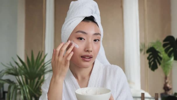 天然化粧品との混合物を作る白いマスク自家製保湿と栄養面マスクやクリームを適用した幸せなアジアの女性がボウルを保持 — ストック動画