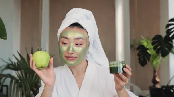 保湿化粧品フェイスマスクでタオルの若いアジアの女性の肖像は 熱帯の背景に緑の物質とリンゴやガラス製品を保持しています スキンケアのための定期的な美容トリートメント — ストック動画