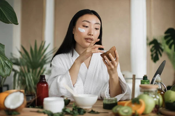 博客或心满意足的创作者亚洲女人在家准备天然化妆品 拿椰子做自制护肤霜 坐在木制桌子旁 有异国情调的家庭温泉 — 图库照片
