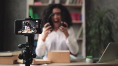 Akıllı telefon ekranına odaklan. Yeni kablosuz kulaklıklarla kutuları açarken kameraya video kaydeden kadın. Abonelerle kadın etkileri paylaşan kişi, yeni düzen hakkındaki olumlu görüşlerini paylaşıyor.