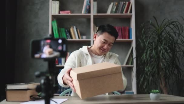 Przystojny Azjata Luźnym Ubraniu Nagrywa Wideo Podczas Rozpakowywania Pudełka Prezentami — Wideo stockowe
