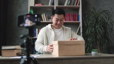 Asyalı adam yeni kablosuz dizüstü bilgisayarla kutusunu açarken kameraya video kaydediyor. Erkek nüfuzlu kişi, abonelerle yeni düzen hakkındaki olumlu görüşlerini paylaşıyor..