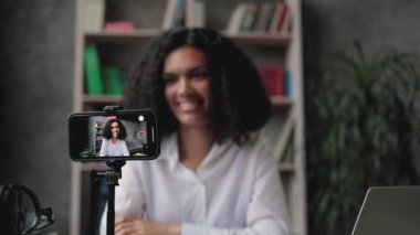 Masasında oturup video blogu çeken, koyu saçlı, oldukça melez bir ırk kadınının bulanık geçmişi. Tripoda sabitlenmiş modern dijital telefona odaklan.