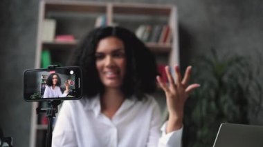 Beyaz tişörtlü Afrikalı Amerikalı kadının sosyal ağları için yeni video blogu kaydettiği bulanık bir geçmişi var. Modern akıllı telefonun kamera ekranına odaklan.