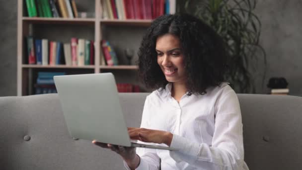 現代のラップトップコンピュータで良いニュースを読んでいる間 ソファに座って幸福からジェスチャー多人種の女性を驚かせた 感情の概念 — ストック動画