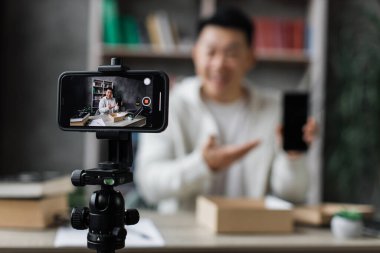 Akıllı telefon ekranına odaklan. Hoş Asyalı adam modern telefon kamerasıyla video çekerken paket kutusunu yeni akıllı telefonuyla açıyor. İnsan kavramı, teknoloji ve blog yazma.