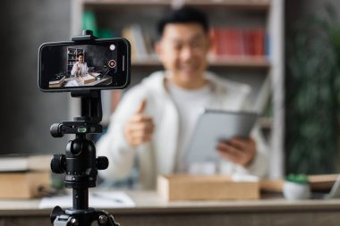 Akıllı telefon ekranına odaklan, Asyalı adam yeni tabletle birlikte kutuyu açarken kameraya video kaydediyor. Genç erkek nüfuz sahibi abonelerle yeni düzen hakkındaki olumlu görüşlerini paylaşıyor.
