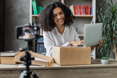 Çok kültürlü bir kadın telefon kamerasıyla video kaydederken yeni kablosuz laptop kutusunu açıyor. Abonelerle kadın etkileri paylaşan kişi, yeni düzen hakkındaki olumlu görüşlerini paylaşıyor.