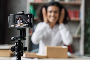 Akıllı telefon ekranına odaklan. Yeni kablosuz kulaklıklarla kutuları açarken kameraya video kaydeden kadın. Abonelerle kadın etkileri paylaşan kişi, yeni düzen hakkındaki olumlu görüşlerini paylaşıyor.