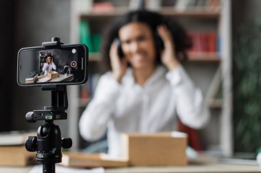 Akıllı telefon ekranına odaklan. Yeni kablosuz kulaklıklarla kutuları açarken kameraya video kaydeden kadın. Abonelerle kadın etkileri paylaşan kişi, yeni düzen hakkındaki olumlu görüşlerini paylaşıyor.