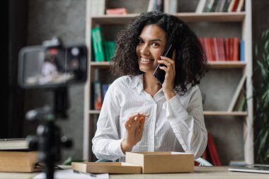 Hoş, çok uluslu bir kadın yeni akıllı telefonuyla paket kutusunu açarken modern telefon kamerasıyla video çekiyor. İnsan kavramı, teknoloji ve blog yazma.