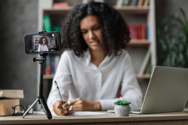 Ekrana odaklan, beyaz gömlekli çok uluslu büyüleyici kadın abonelerle konuşurken aynı zamanda rapor yazıyor ve tripodla modern telefondan video kaydediyor..