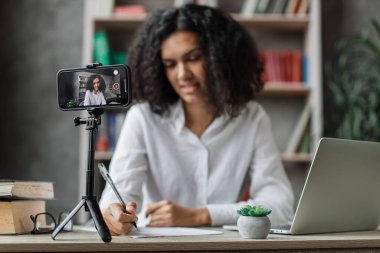 Ekrana odaklan, beyaz gömlekli çok uluslu büyüleyici kadın abonelerle konuşurken aynı zamanda rapor yazıyor ve tripodla modern telefondan video kaydediyor..
